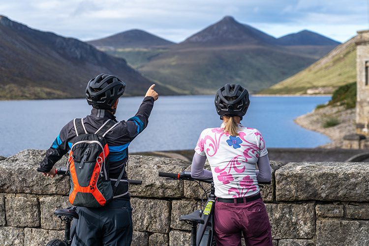 Man and woman admiring the views of Silent Valley, standing on top of the dam and looking towards the beautiful Mourne Mountains